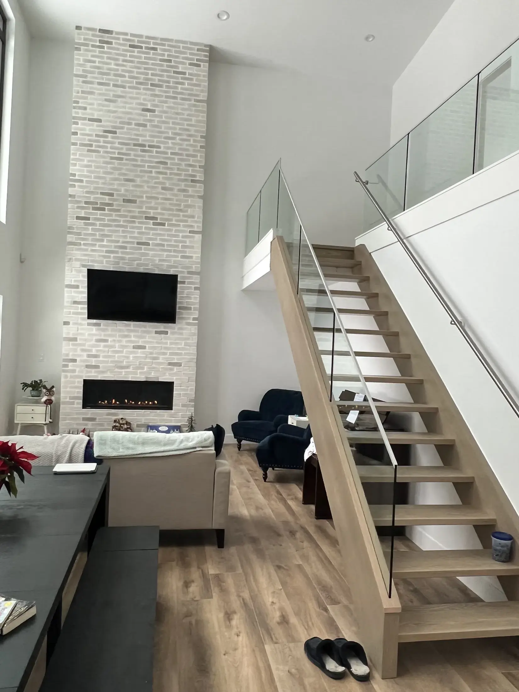 Two-story living room with tiled gas fireplace, mounted TV, and open-tread stair with glass railing.